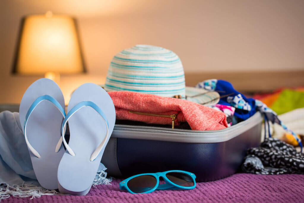 Typical packing list for Hawaii in October, includes shorts and light clothing. Image shows a suitcase with blue flip flops, sunglasses, and a hat.