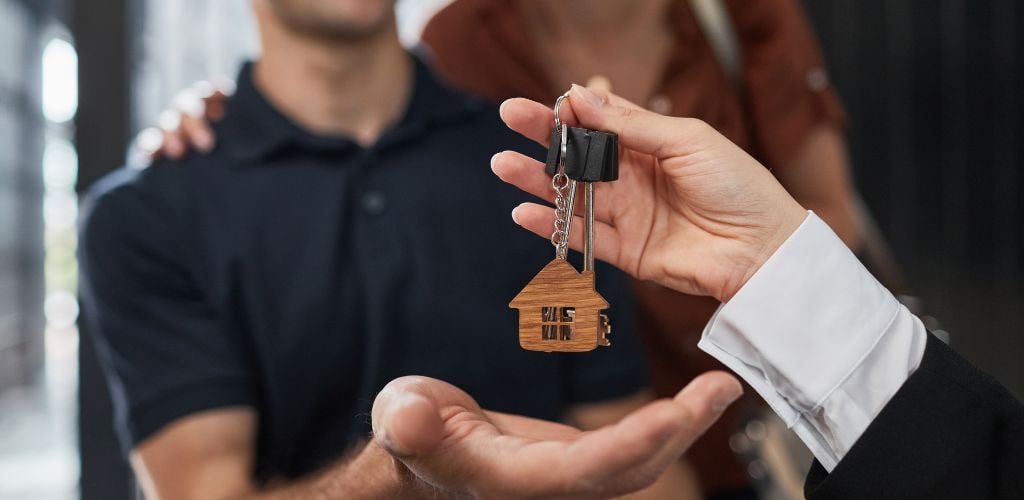 A woman handing over house keys to a couple.