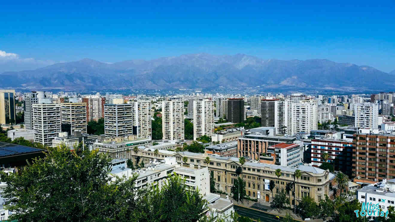 A panoramic view of Santiago de Chile displaying tall buildings against a backdrop of mountains under a clear blue sky.