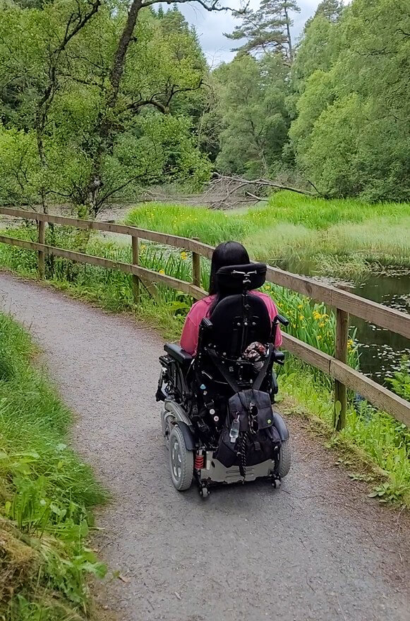 Emma in her powered wheelchair driving along a hard surface path in Faskally Woods.