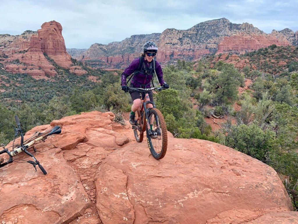 Mountain biker riding bike up red rock slab in Sedona with dramatic backdrop