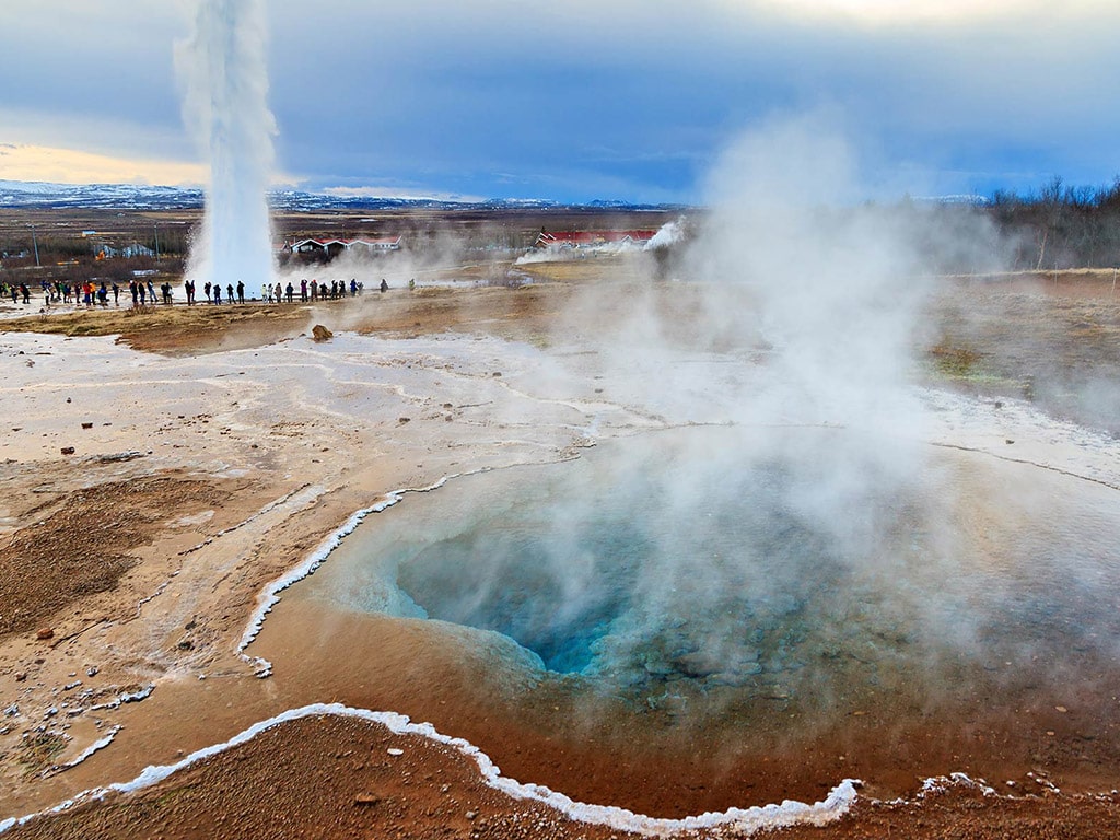 Steam rises from a turquoise geothermal pool near an erupting geyser at the Strokkur geyser field in Iceland.