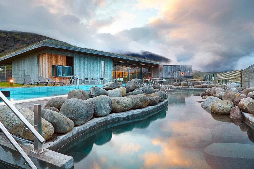 Geothermal pools surrounded by rocks and modern buildings at Laugarvatn Fontana Spa, complemented by a peaceful sunset sky in Iceland.