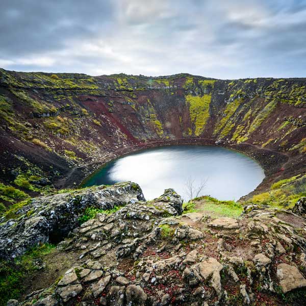 View of the Kerid volcanic crater filled with a serene blue lake, surrounded by moss-covered slopes in Iceland.