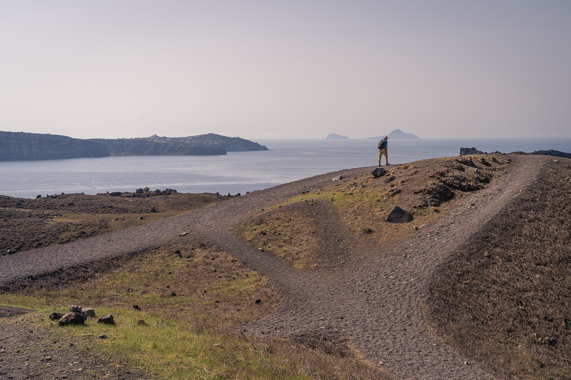 This image shows a man walking on the bare slopes of Santorini's volcano.