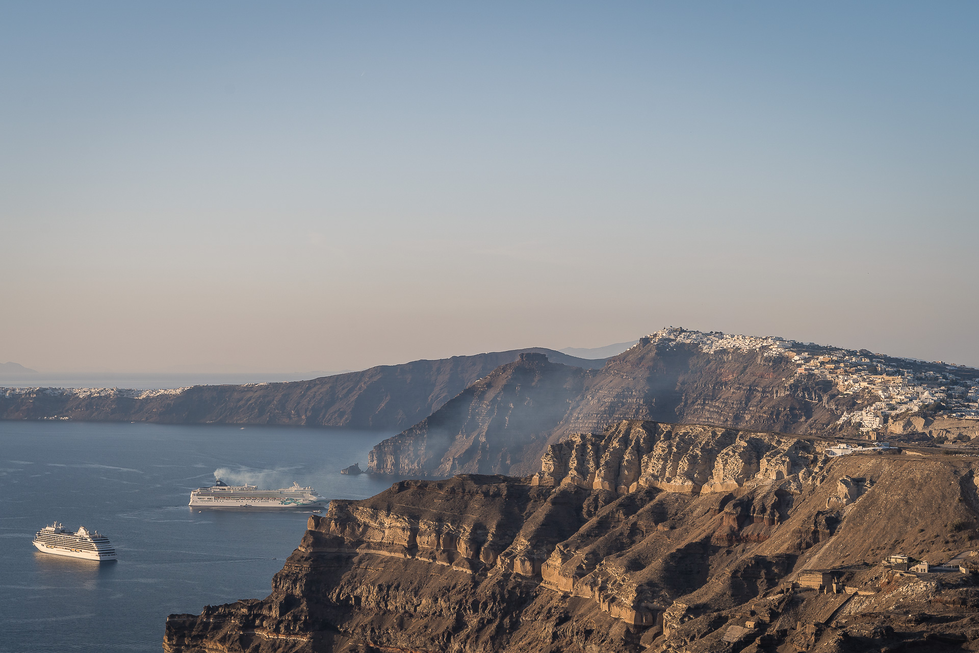 This image shows Santorini's caldera with two cruise ships in the sea. If you want to support ecotourism in Santorini, don't visit Santorini on a cruise.