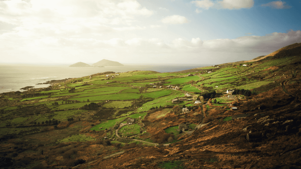 Rolling green hills meet the sea under a cloudy sky.