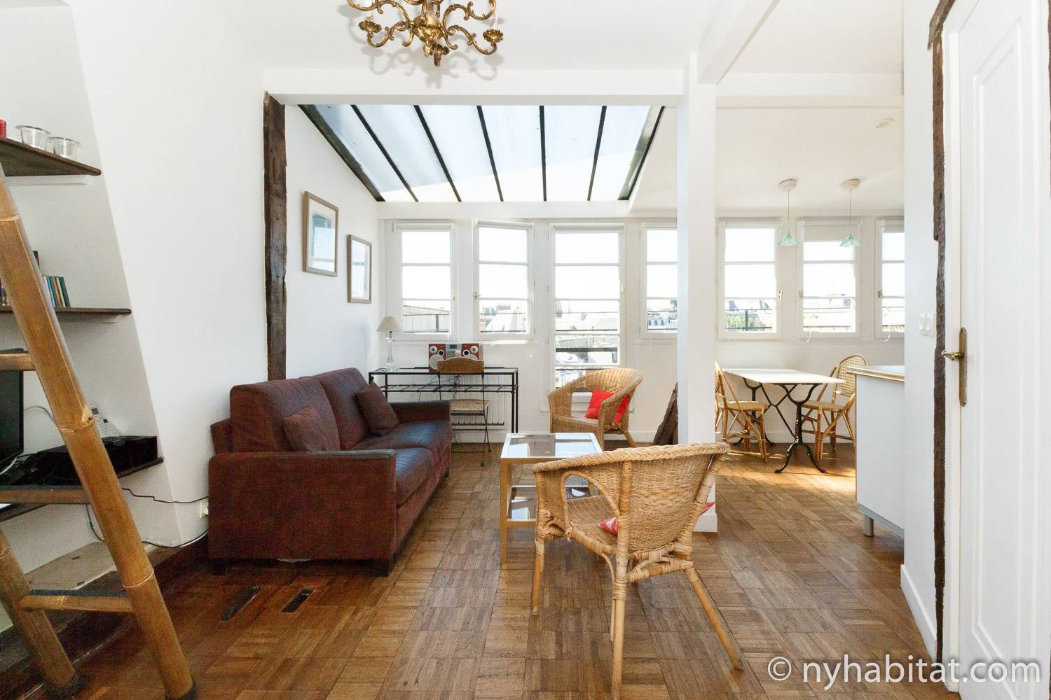 Living room of furnished apartment PA-2473 in Saint-Germain des Prés, showcasing a door leading to the balcony in the background, with multiple windows and a skylight.