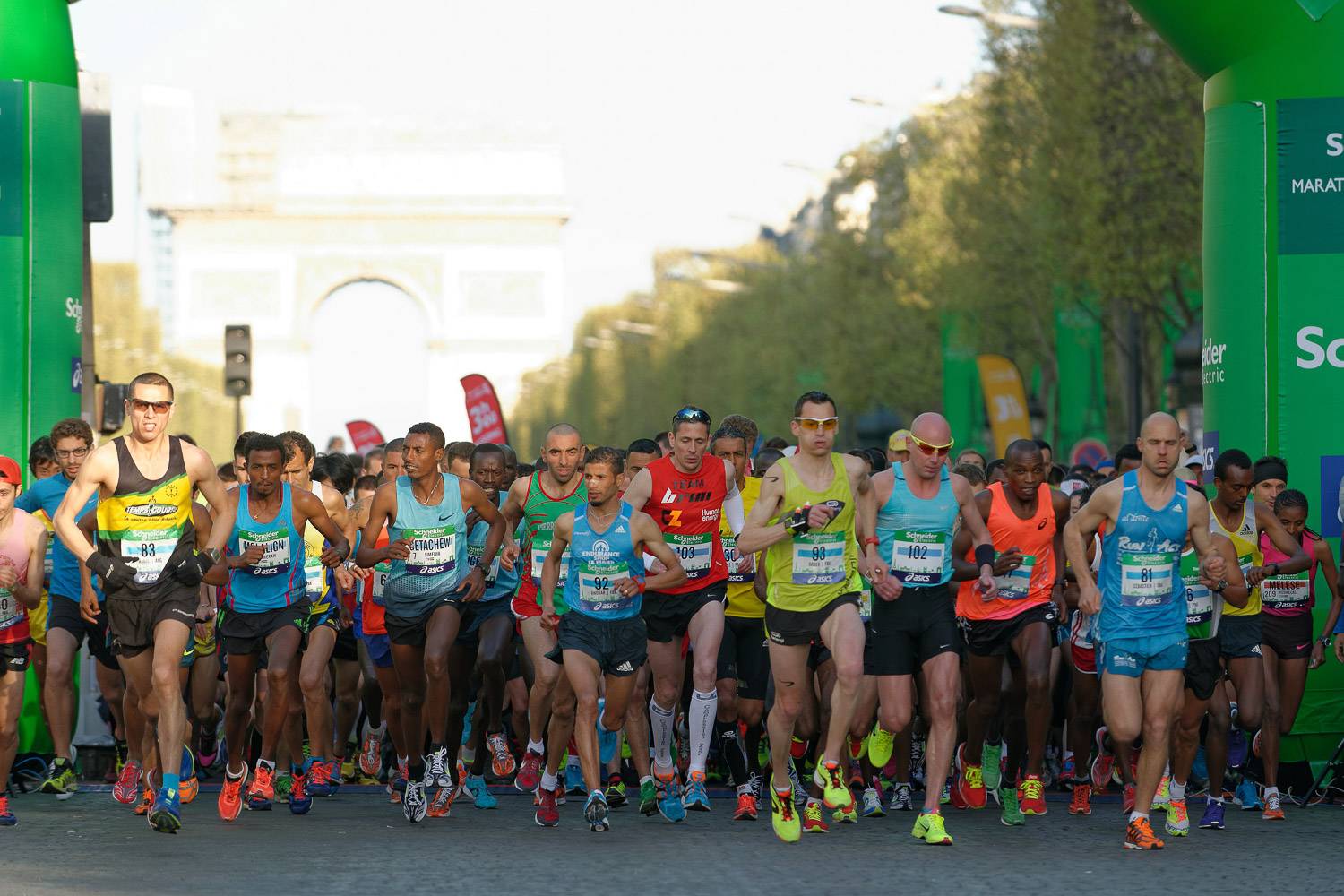 Participants of the Paris Marathon running along the Champs-Elysées Avenue with the Arc de Triomphe in the background.