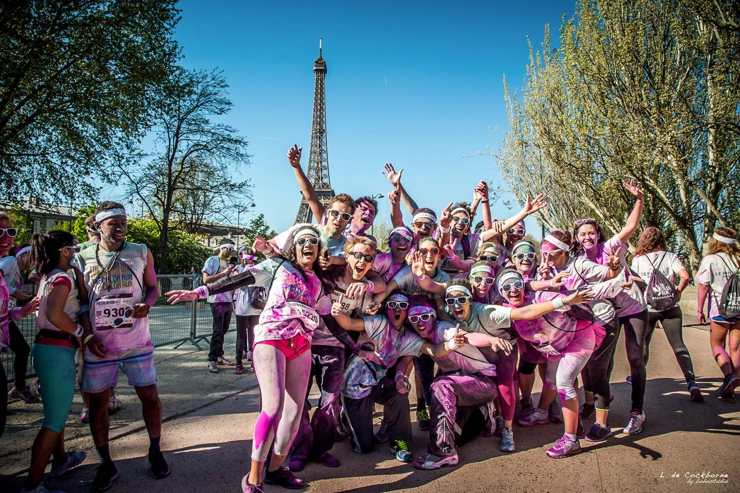 A group of Color Run participants in Paris, splashed with colorful powders against the backdrop of the Eiffel Tower.