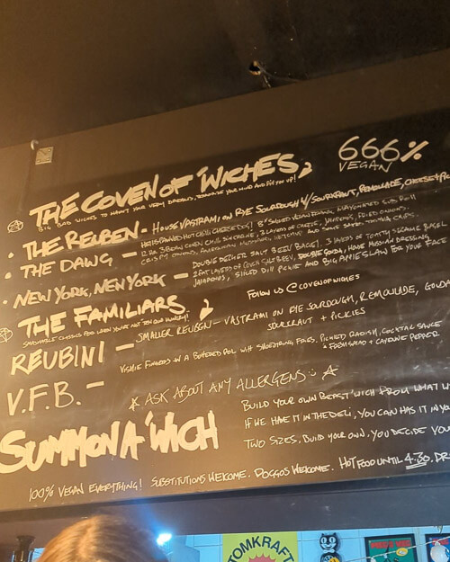 A black chalkboard menu at Coven of Wiches detailing their plant-based sandwich offerings.