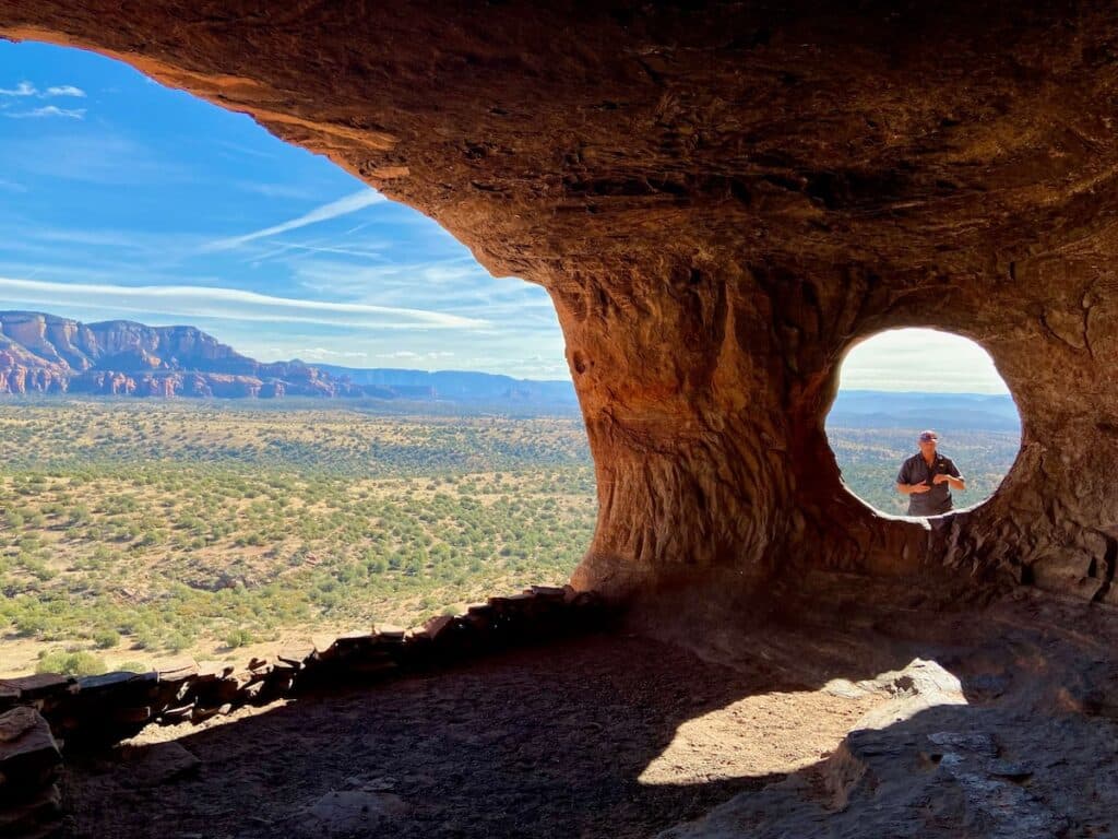 Man standing in frame of circular hole in red rock cave at Robbers Roost in Sedona