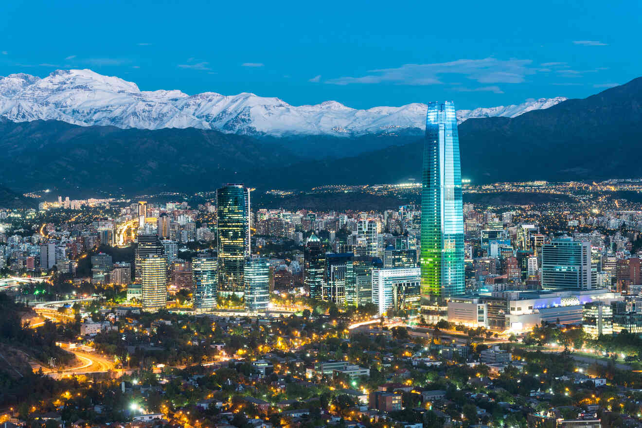 Santiago de Chile skyline at dusk showcasing illuminated skyscrapers and the snow-capped Andes Mountains in the background.