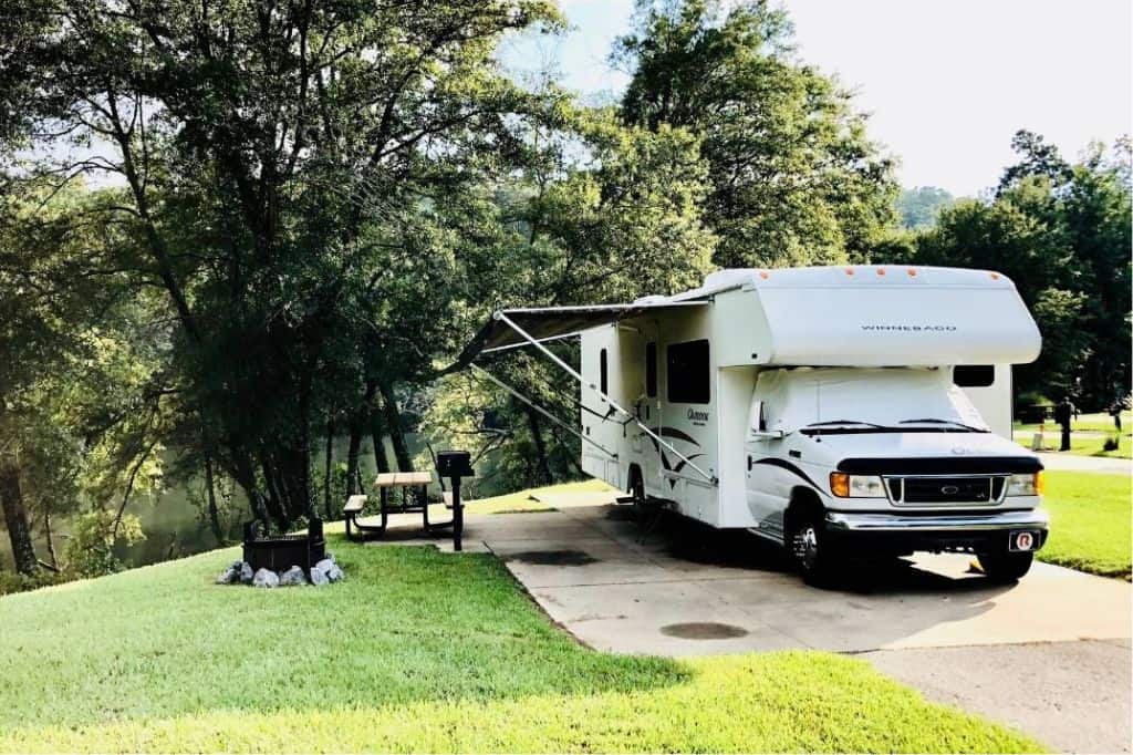 A motorhome parked next to a tree and picnic table