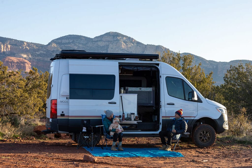 Two people sitting in camp chairs outside a Storyteller Sprinter van